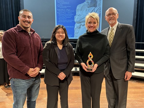 Four people standing on stage smiling for a photo. One woman is holding an award.