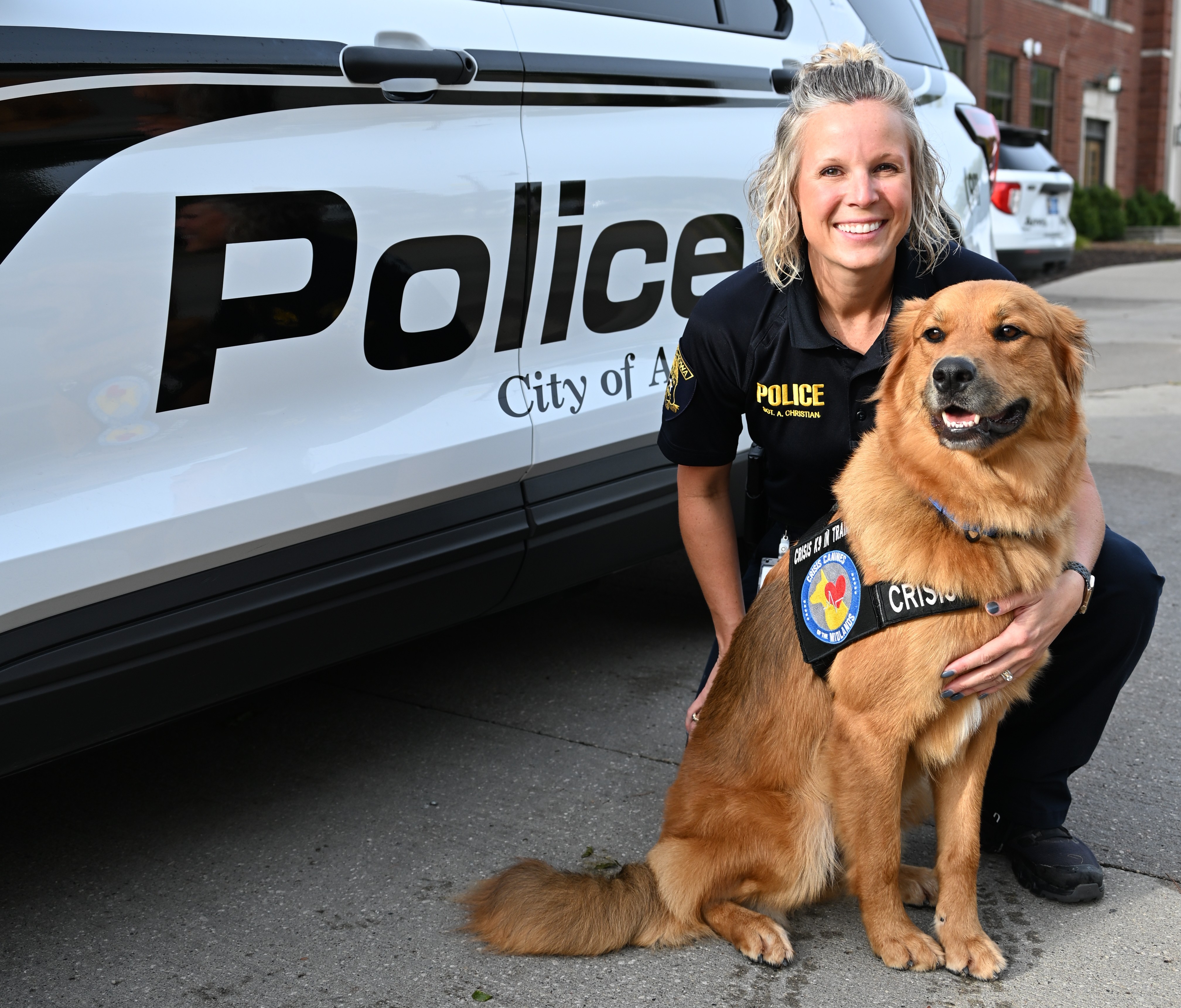 Dog with police officer in front of a police car