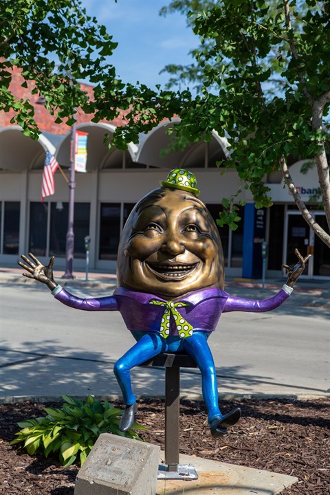 Bronze egg dressed in a green hat with a purple shirt and blue pants