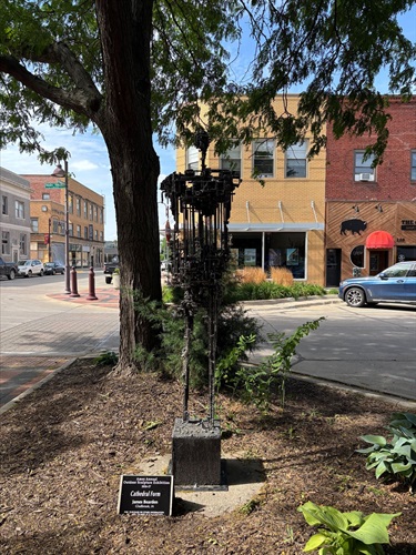 tall metal sculpture features an intricate, open framework rising from a square pedestal